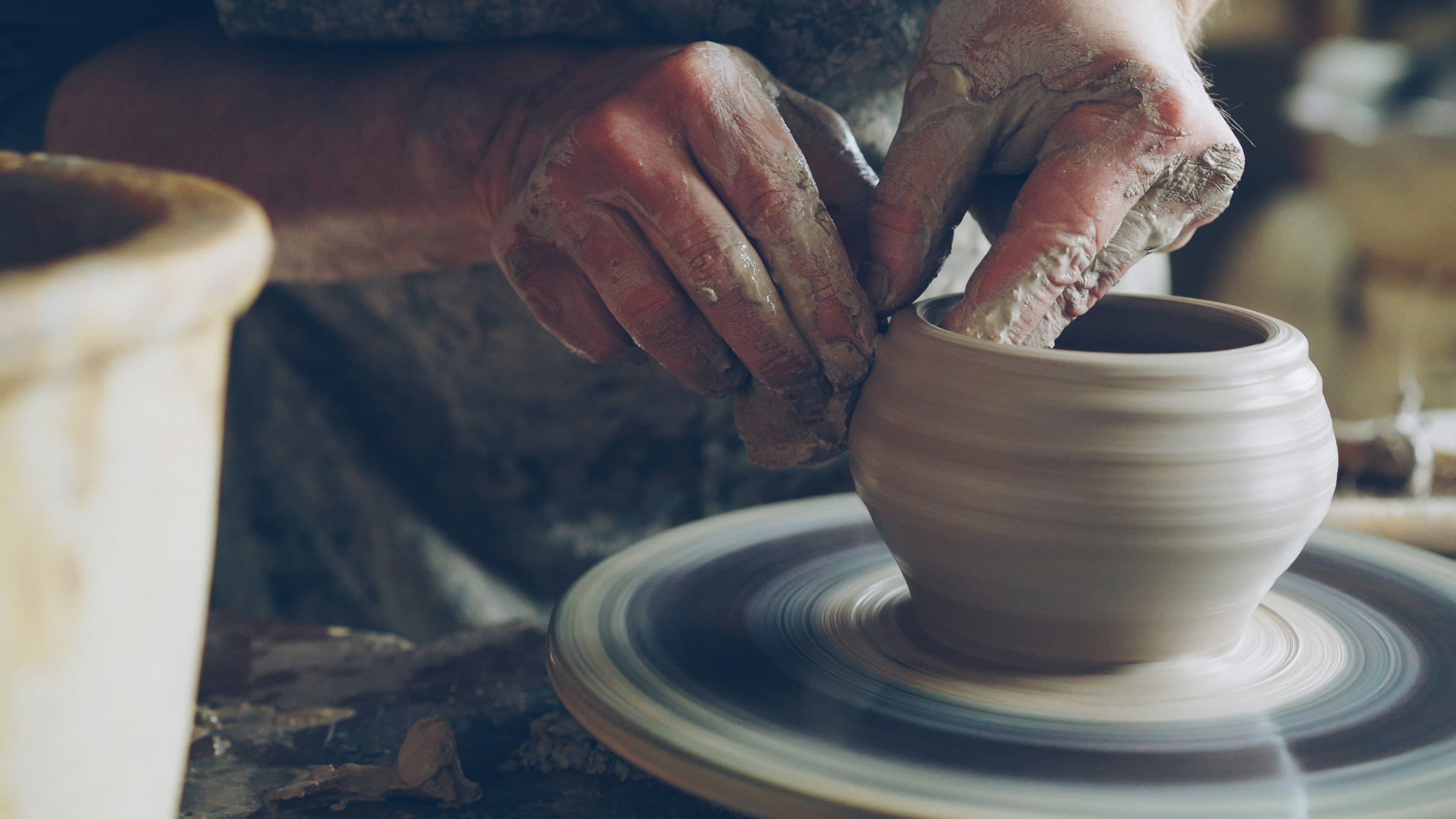 Hands shaping a clay pot on a pottery wheel